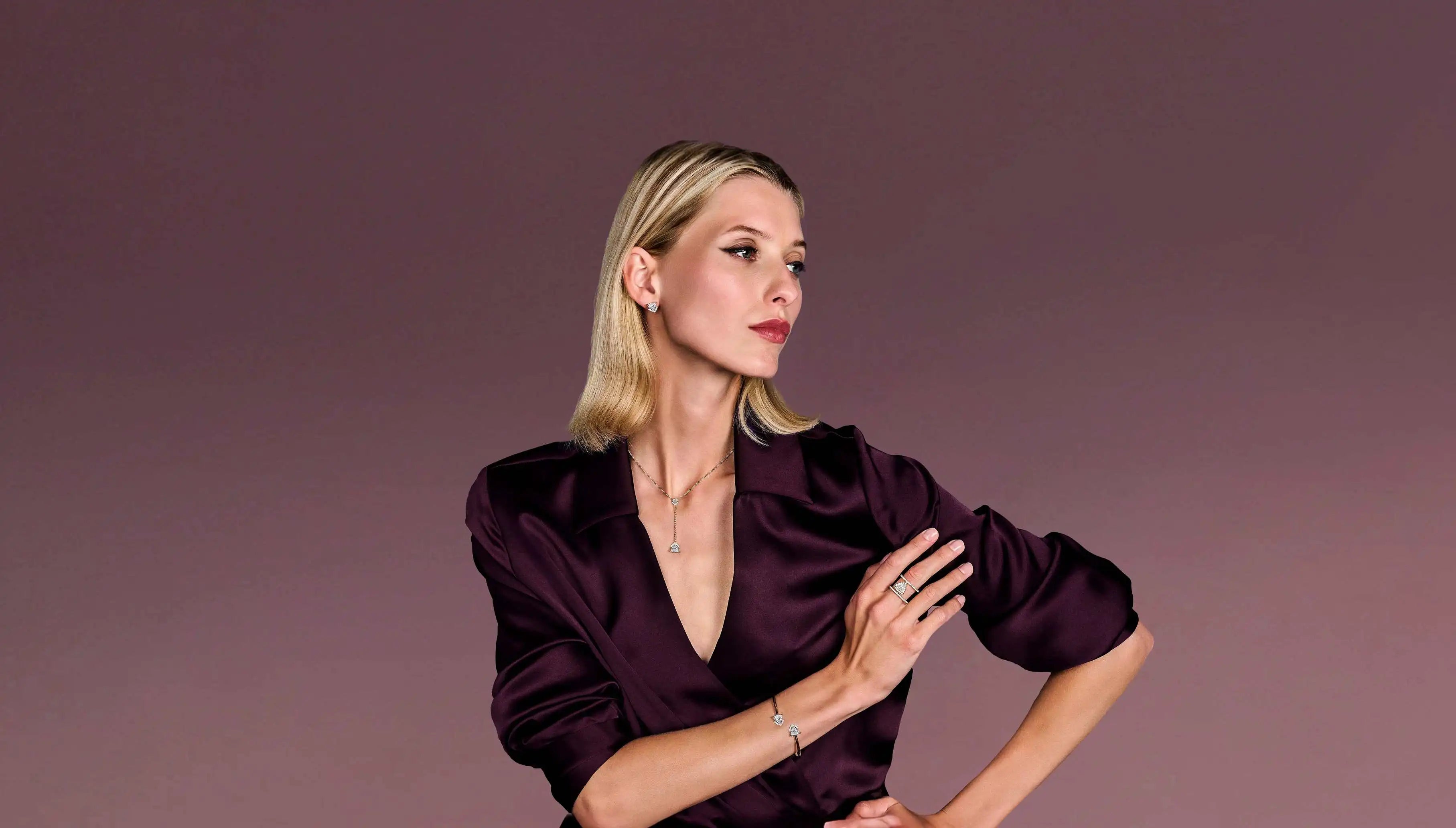 Woman stacking lab-grown fine jewellery pieces from Okker & Ockers behind a rose backdrop.