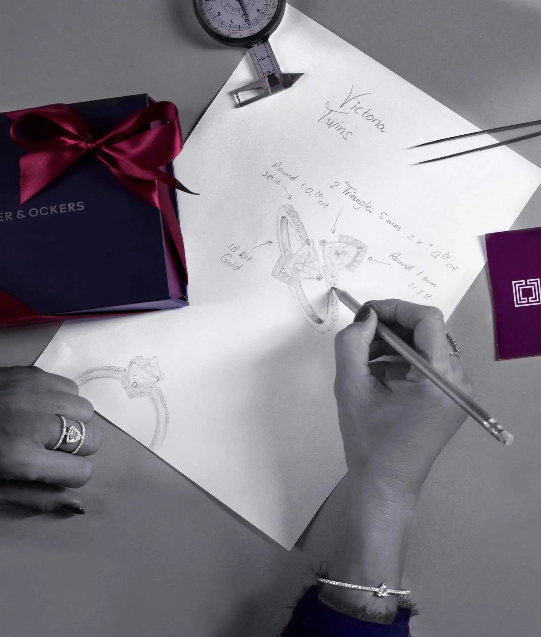 Our designer sketching jewellery designs, working on the Victoria Twins ring concept. A gift box, caliper, and design notes surround her workspace.