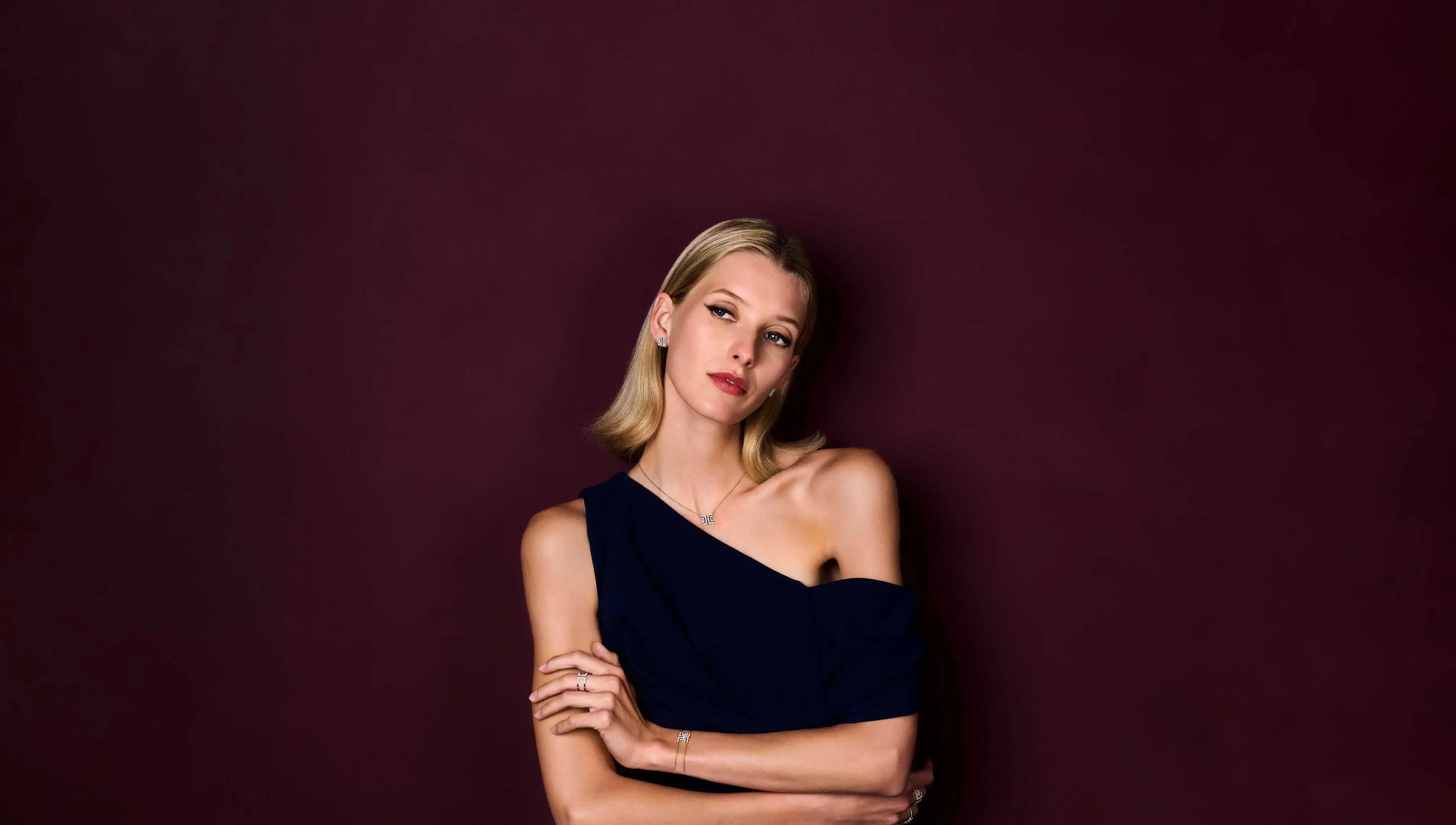 Model wearing the fine jewellery from the Entre-Deux collection posing against an aubergine-coloured backdrop.
