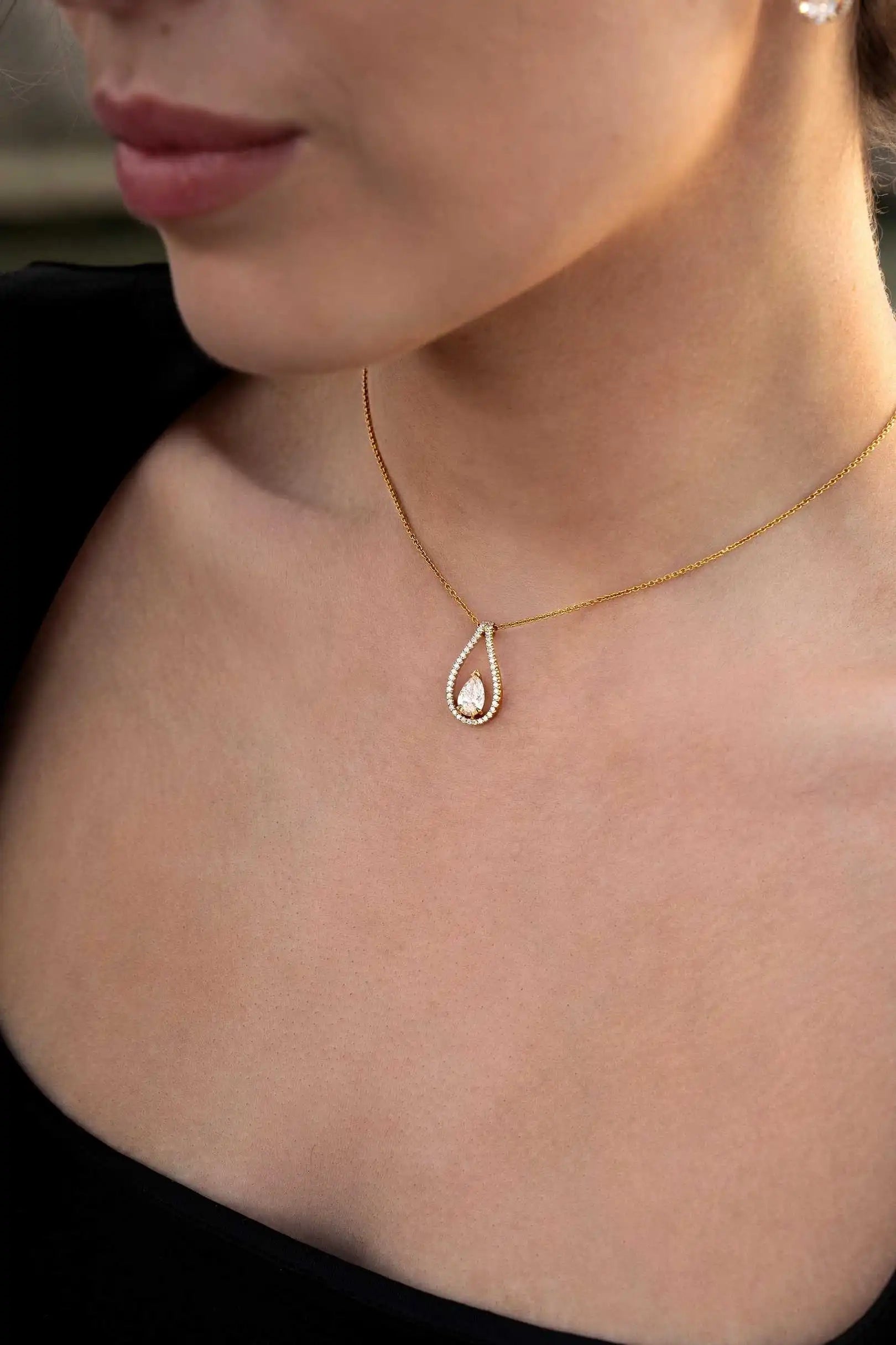 Close-up of the Floating Pendant necklace resting on the model's neckline, featuring a pear-cut diamond in a diamond-set halo.