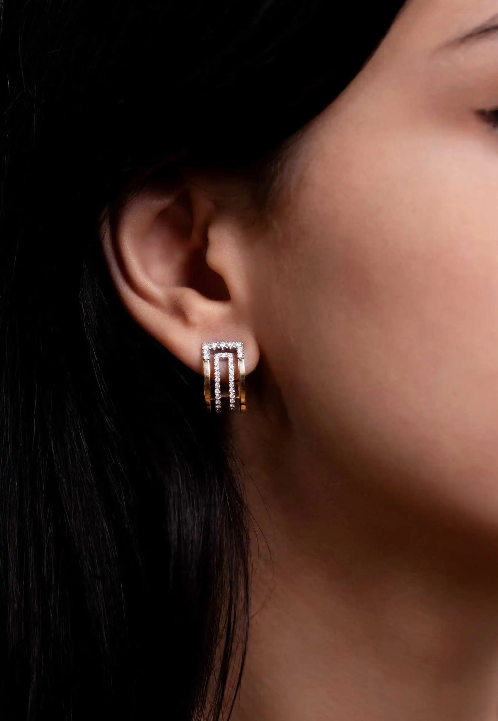 Close-up of a model wearing the Heloise Arcs earrings, featuring a bi-colour gold design with diamond-studded geometric curves.
