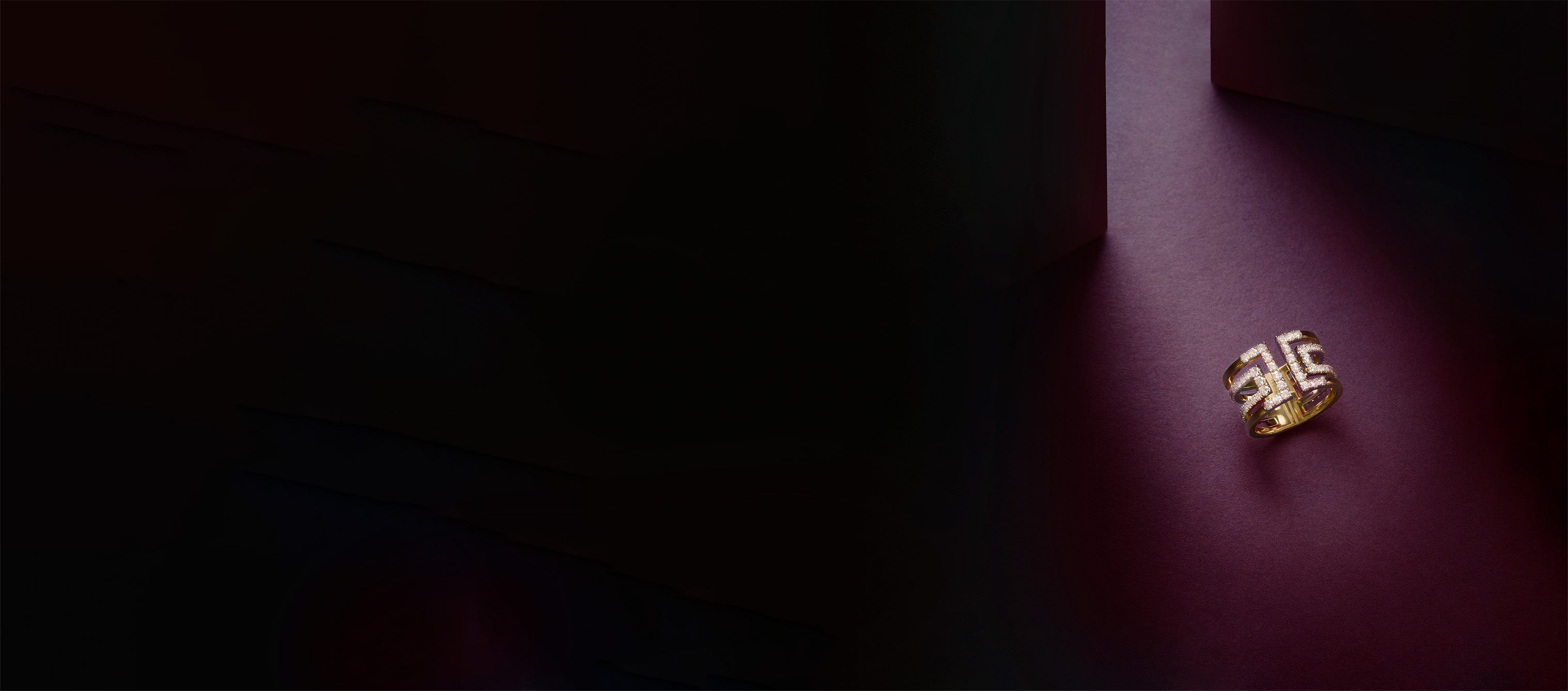 Harper Icon ring in yellow gold, illuminated by a dramatic beam of light on a deep aubergine surface.
