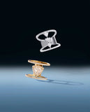The Davina Icon ring in white gold and the Audrey Icon ring in yellow gold from the Les Angles collection, visibly floating in mid-air. Both designs feature striking triangle-cut lab-grown diamonds, set in architectural castle settings, casting soft shadows against a gradient blue background.